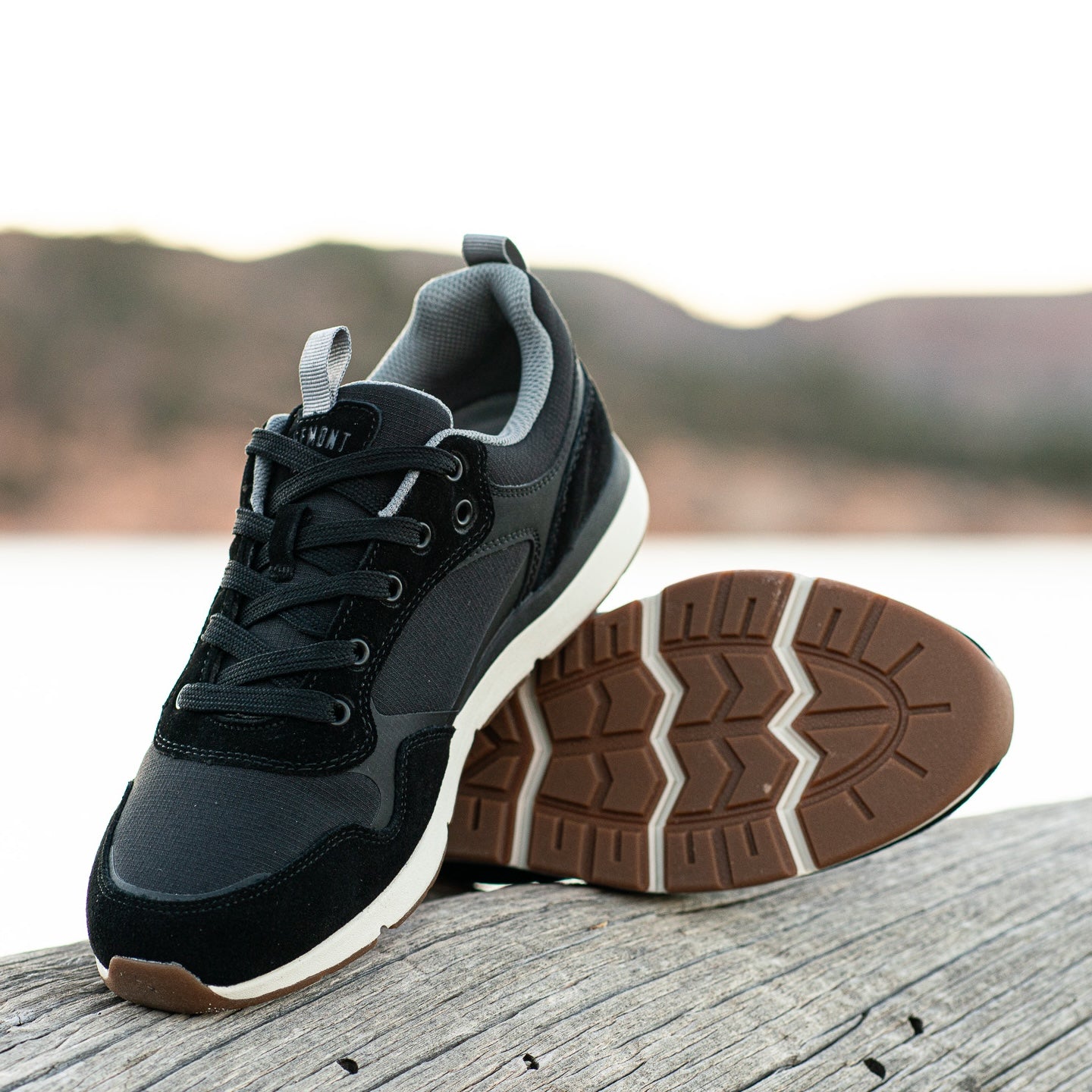Pair of Escape sneaker shoe in color Black in St George, Utah. Propped shoe shows black canvas, black ripstop poly, black oil suede, black laces, CMEVA white midsole, and grey inner lining. Shoe lying on side shows real rubber tread in color gum. Shoes are laying on wood outside. Active footwear. Everyday sneakers. Comfortable shoes. Everyday shoe. Ridgemont x St George. Ridgemont shoe x water. Black Escape.