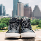 Pair of Ridgemont Outback boot in colors Black Grey with black laces and white foxing. Front view of shoes in city landscape. Taken outdoors in Austin, Texas.