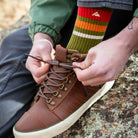 Person wearing a Ridgemont Trailblazer sock tieing up his laces of a Ridgemont Outback boot in Brown Olive while sitting on a boulder