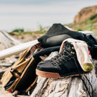 Ridgemont Monty Black Gum outdoor shoe resting on driftwood at San Onofre beach with wetsuit, backpack and surfboard.