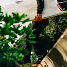 Surfer wearing Ridgemont Black Gum Monty stepping over wall barrier with Firewire Surfboard on way to beach
